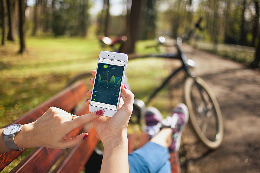 Radfahrende sitzt auf Parkbank und trägt Kilometer über die Stadtradeln App ein